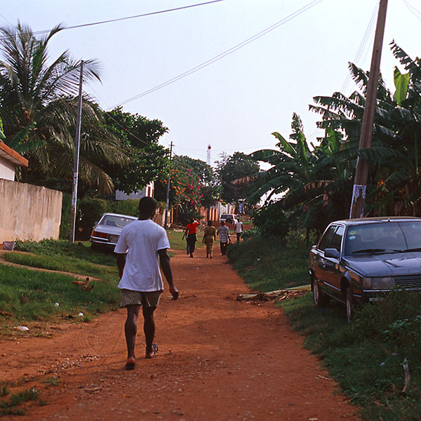 Young Ghanaian teen walks down dirt path in rural town.